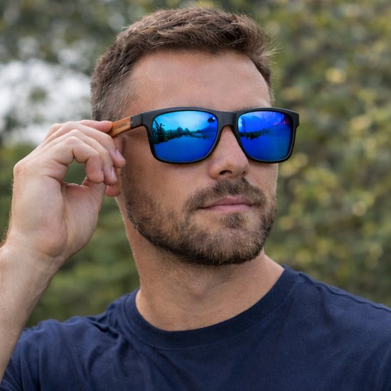 Man met zwarte bril met houten pootjes. De blauw spiegelende glazen reflecteren een landschap.