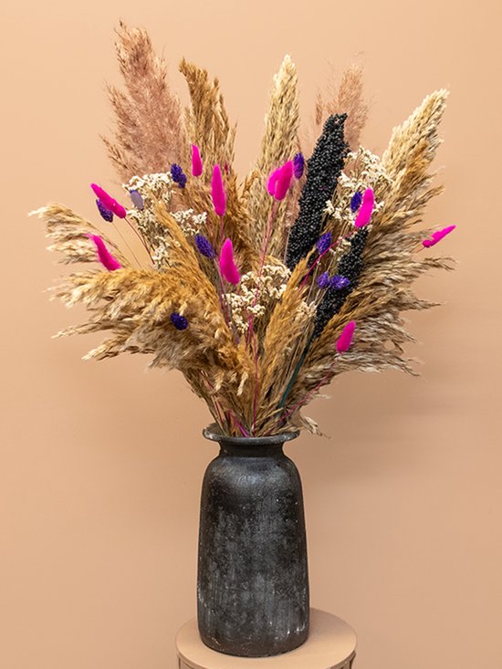 Boeket van pampasgras, felroze en paarse bloemen en donkere bessen in een donkergrijze vaas.