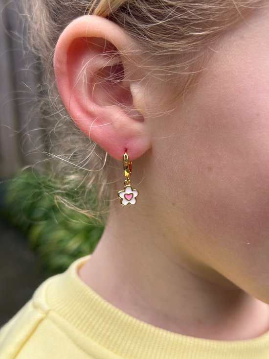 Gouden oorringetje met een witte bloem met roze hartje, gedragen door een meisje.
