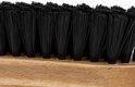 Gros plan sur les poils noirs d'une brosse de nettoyage sur une base en bois.