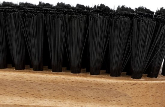 Gros plan sur les poils noirs d'une brosse de nettoyage sur une base en bois.