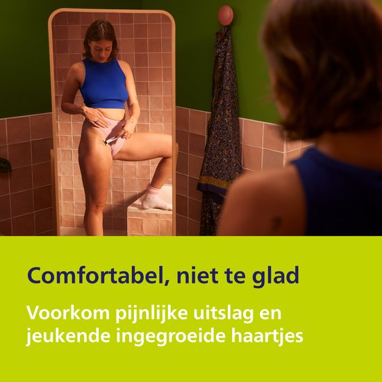 Vrouw met scheerapparaat in de hand, kijkt naar zichzelf in de spiegel.