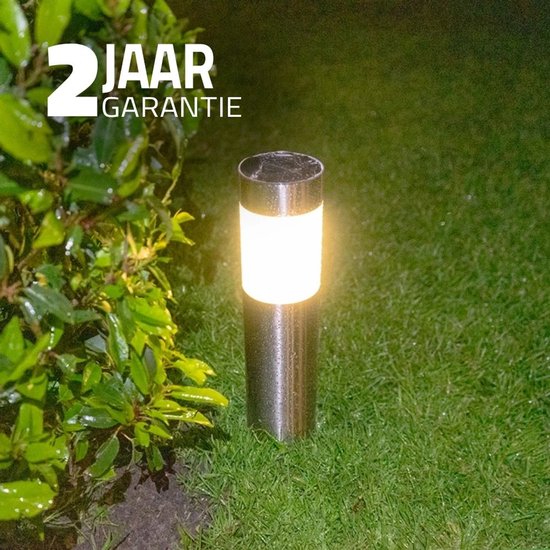 RVS solar tuinlamp met een heldere, witte lichtkap, staand in het gras. Twee jaar garantie vermeld.