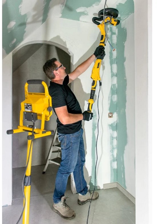 Man schuurt een plafond met een gele en zwarte telescoopschuurmachine.