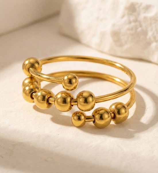 Gouden spiraalring met schuifbare balletjes op een lichte ondergrond.