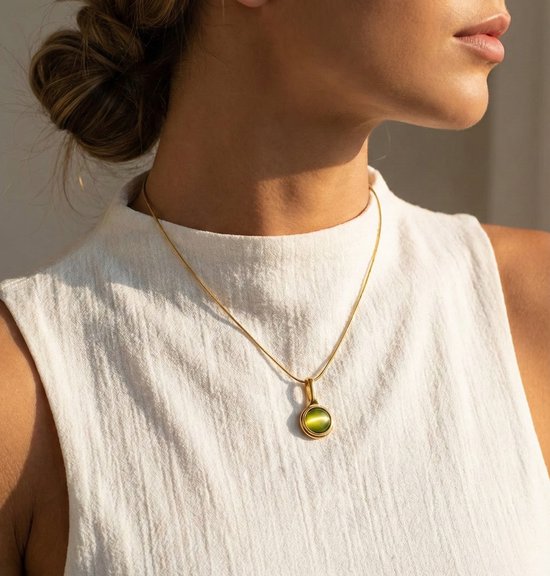 Collier doré avec une petite pierre ronde verte, porté par une femme.