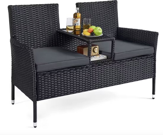 Zwarte rotan 2-zits bank met middenconsole, kussens en decoraties. Inclusief fles, fruit en boek.