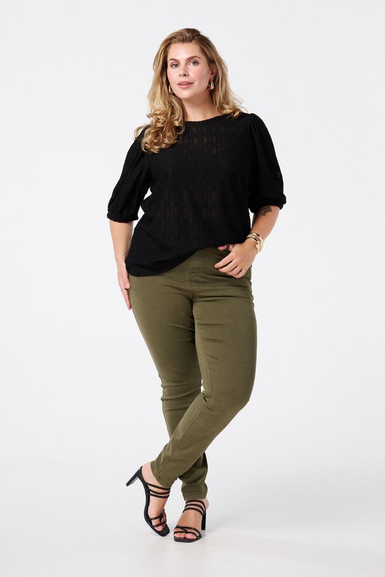 Model draagt een zwarte top en olijfgroene skinny tregging.