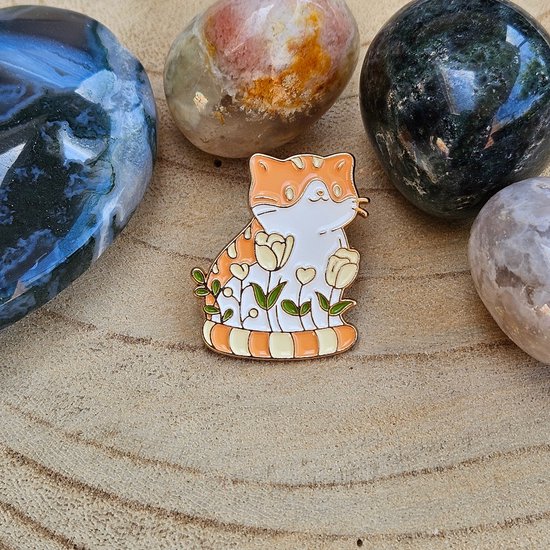 Chat orange et blanc avec queue rayée et motif floral, entouré de pierres
