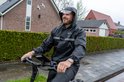 Man op een fiets in de regen, draagt een zwarte regenjas met capuchon en reflecterende strepen. De jas heeft het "VOLTANO" logo.
