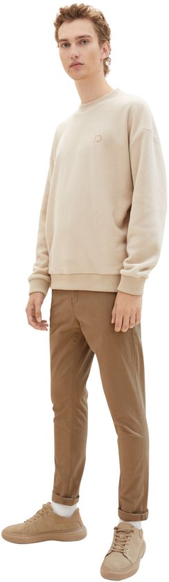 Model met bruine chino broek en beige trui.