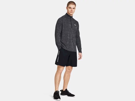 Man in zwart sportshirt met halve rits en zwart sportbroekje met logo op linkerbeen.