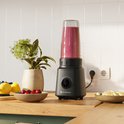 Zwarte KitchenBrothers blender met een kan gevuld met smoothie, op een aanrecht met fruit.