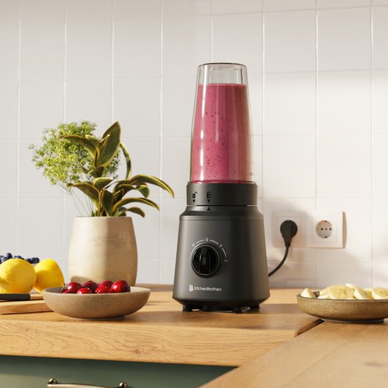 Zwarte KitchenBrothers blender met een kan gevuld met smoothie, op een aanrecht met fruit.