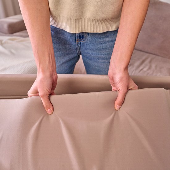 Een vrouw houdt een beige stof vast, de rand van een reisbedje.