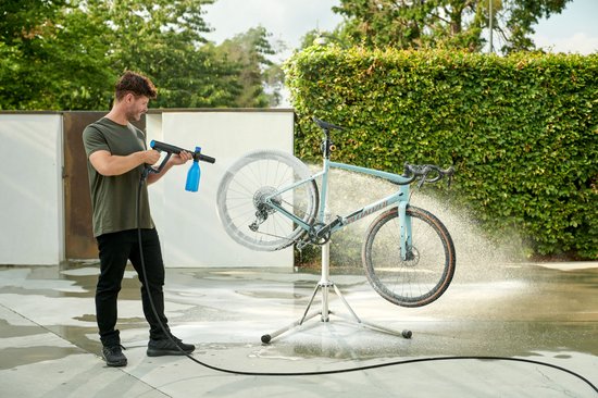 Man met donkergroene t-shirt reinigt een lichtblauwe fiets met een Nilfisk hogedrukreiniger.