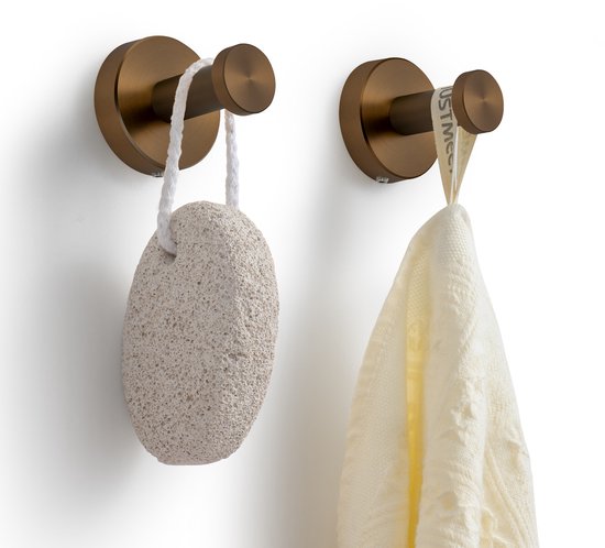 Koperkleurige handdoekhaak met een puimsteen aan het ene haakje en een witte theedoek aan het andere.