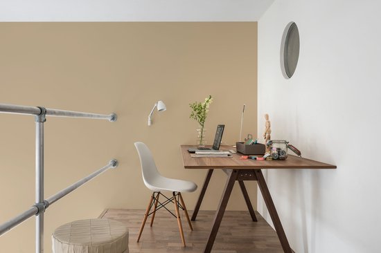 Bureau met laptop en witte stoel met houten poten, naast een metalen leuning en beige muur.