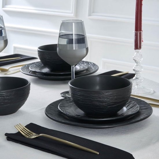 Tafelsetting met zwarte borden, kommen, gouden bestek en glas.