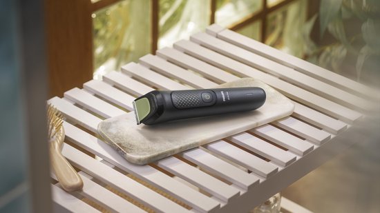 Zwarte Philips All-in-One trimmer op een marmeren onderzetter op een houten rekje, naast een borstel.