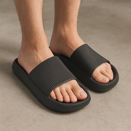 Voeten in zwarte slippers. Duidelijk zicht op de dikke zool en het geribbelde bovenwerk.