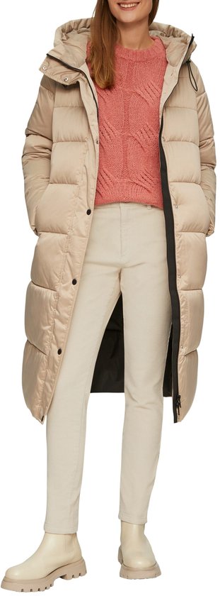 Model in een lange beige pufferjas over een roze trui en crèmekleurige corduroy broek, met beige laarsjes.
