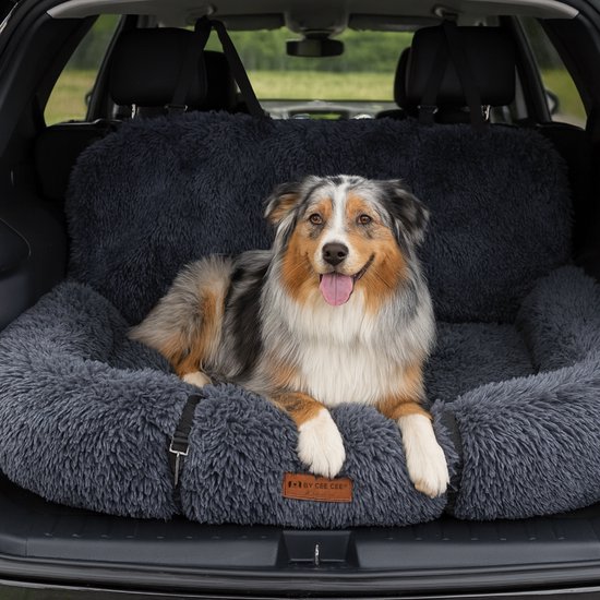 Een Australische herder met open mond ligt op een donkergrijs, pluizig hondenbed in de kofferbak van een auto.