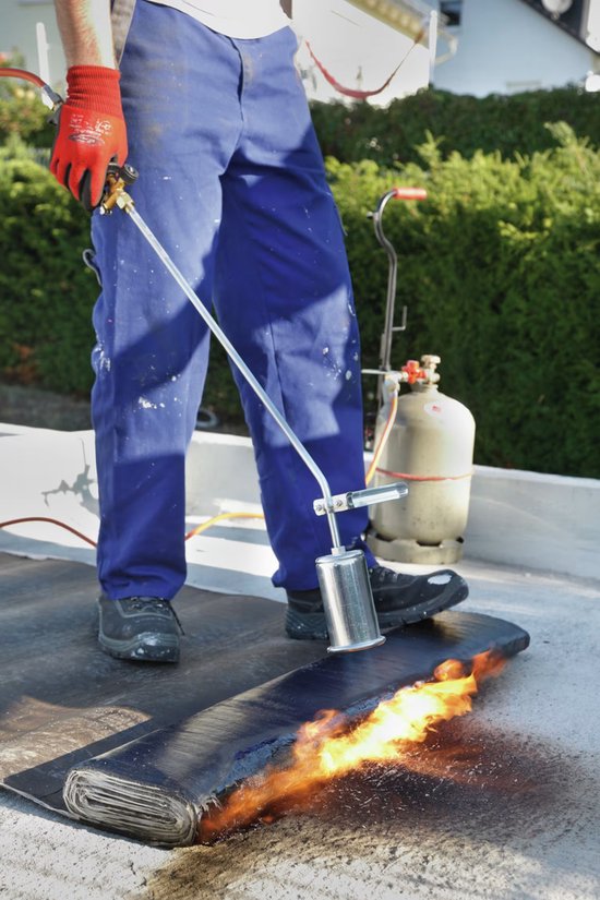 Man met rode handschoenen en blauw werkpak gebruikt brander op zwarte dakrol met vlammen.