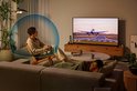 Man luistert naar audio met nekband speaker en blauwe geluidsgolven om hem heen.