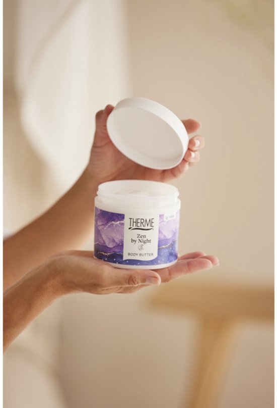 Handen houden een pot Therme Zen by Night bodybutter open. Pot heeft een paars, blauw en goudkleurig design.