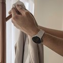 Mannelijk pols met een smartwatch en een crèmekleurig siliconen horlogebandje met golvend patroon, wordt om jas gehangen.