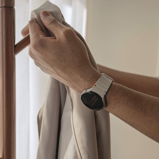 Mannelijk pols met een smartwatch en een crèmekleurig siliconen horlogebandje met golvend patroon, wordt om jas gehangen.