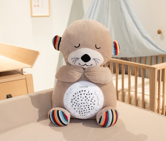Beige otter knuffel zit rechtop in een kamer, met op de buik een sterrenprojector.