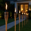 Rij van brandende bamboe fakkels verlichten een tuinpad naast een modern huis.