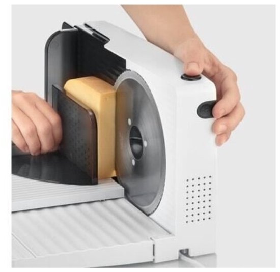Handen plaatsen een blok kaas op de witte snijmachine met zilveren mes.