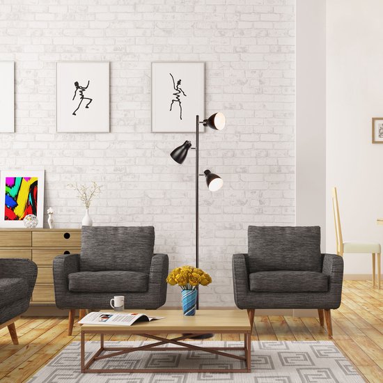 Zwarte staande lamp met drie spots staat in een woonkamer naast een grijze fauteuil.