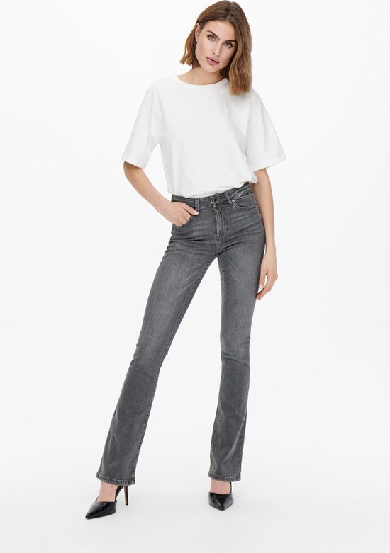 Model in grijze flared jeans en witte T-shirt met zwarte pumps.