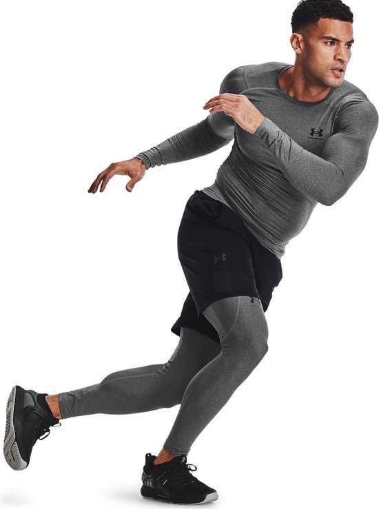 Man die rent in grijze Under Armour tight fit longsleeve met zwart Under Armour logo, zwarte shorts en grijze legging.