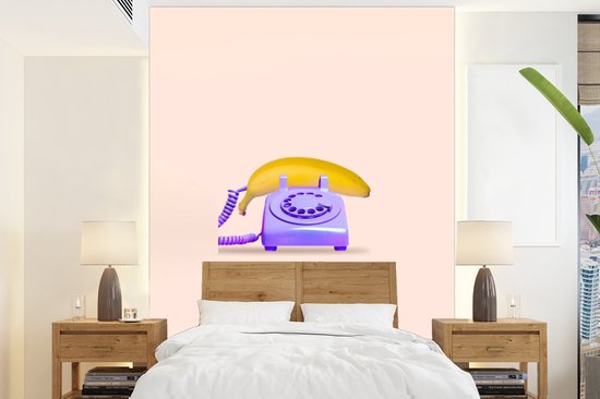 Paarse telefoon met gele banaan op roze achtergrond, boven een houten bed.