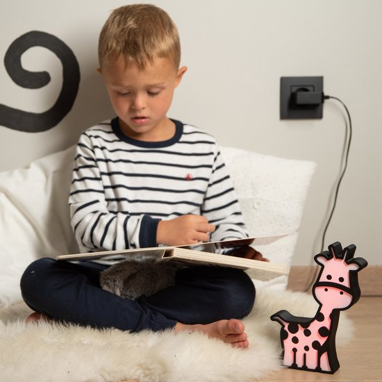 Roze oplichtend giraf-nachtlampje naast een jongen die een boek leest.