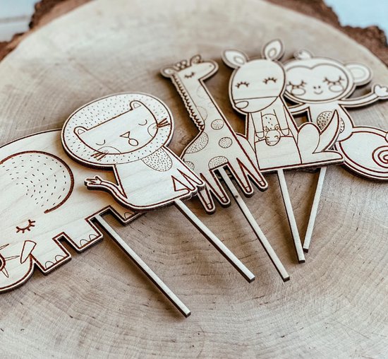 Houten taarttoppers met dierenfiguren: olifant, leeuw, giraf, hert, aap en slak, op een houten ondergrond.