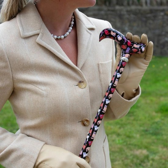 Vrouw in beige jas en parelketting met wandelstok met veelkleurige kattenprint.