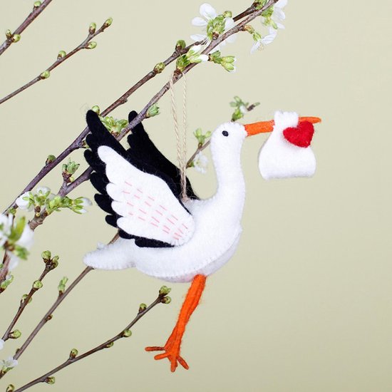Witte ooievaar van vilt met oranje poten en snavel, zwart met wit. Draagt een wit pakketje met rood hart.