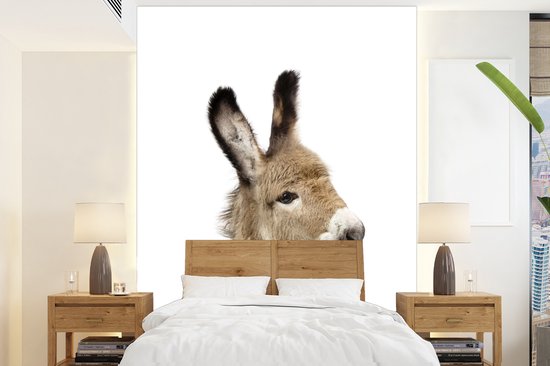 De kop van een jonge ezel met bruine vacht en lange, spitse oren, boven een houten hoofdeinde in een slaapkamer.