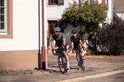 Man en vrouw fietsen buiten. Man draagt olijfgroen shirt, vrouw draagt zwart shirt.