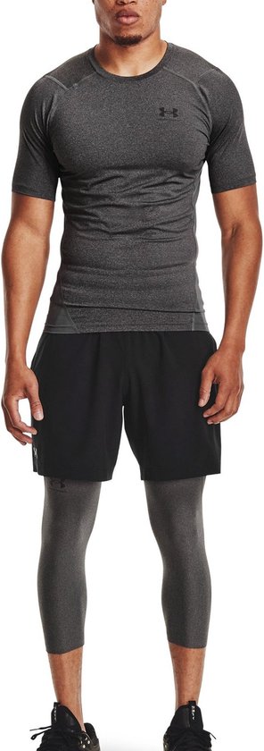 Man met donkergrijs, aansluitend sportshirt met korte mouwen, zwarte shorts en grijze driekwart leggings.