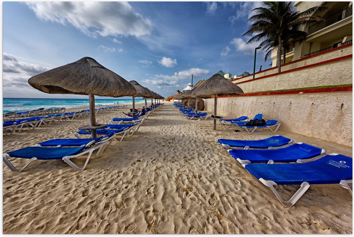 Poster (Mat) - Blauwe Ligbedden op Strand met Rieten Parasols - 105x70 cm Foto op Posterpa