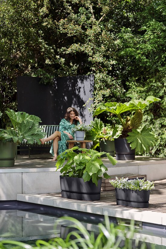 Een vrouw zit op een bank in een tuin bij twee zwarte plantenbakken.