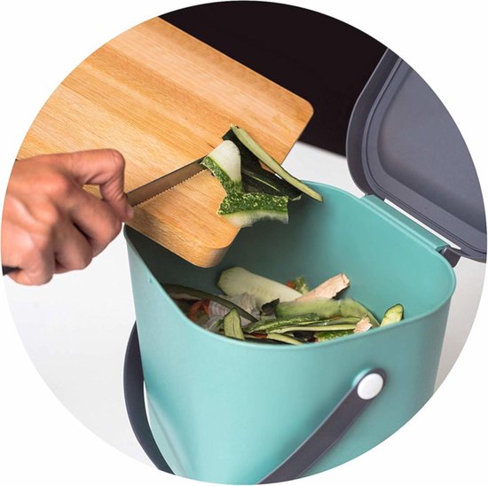 Groene afvalbak met groen deksel. Een hand met een mes schraapt groenteafval van een snijplank.
