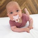 Baby met een roze Difrax fopspeen op een witte ondergrond.